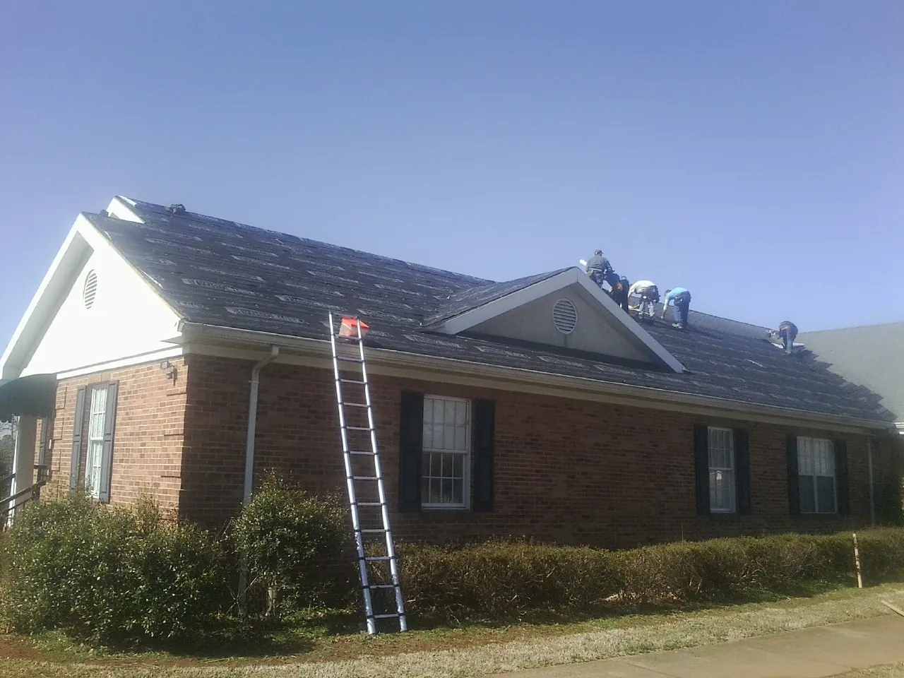 Crew tearing shingles off a brick ranch roof with a ladder set — Emergency Roof Repair work by our crew in Cheyenne