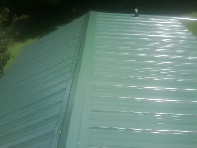 New green metal panels meeting at the ridge of a roof — Flat Roof Repair work by our crew in Cheyenne