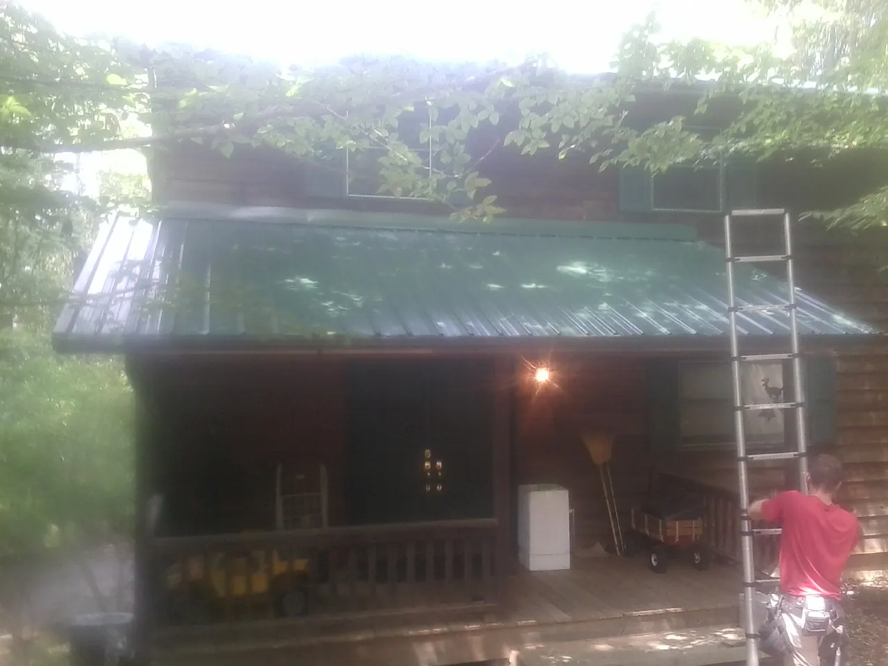 Worker on a ladder at the green porch roof of a wooded cabin in Cheyenne