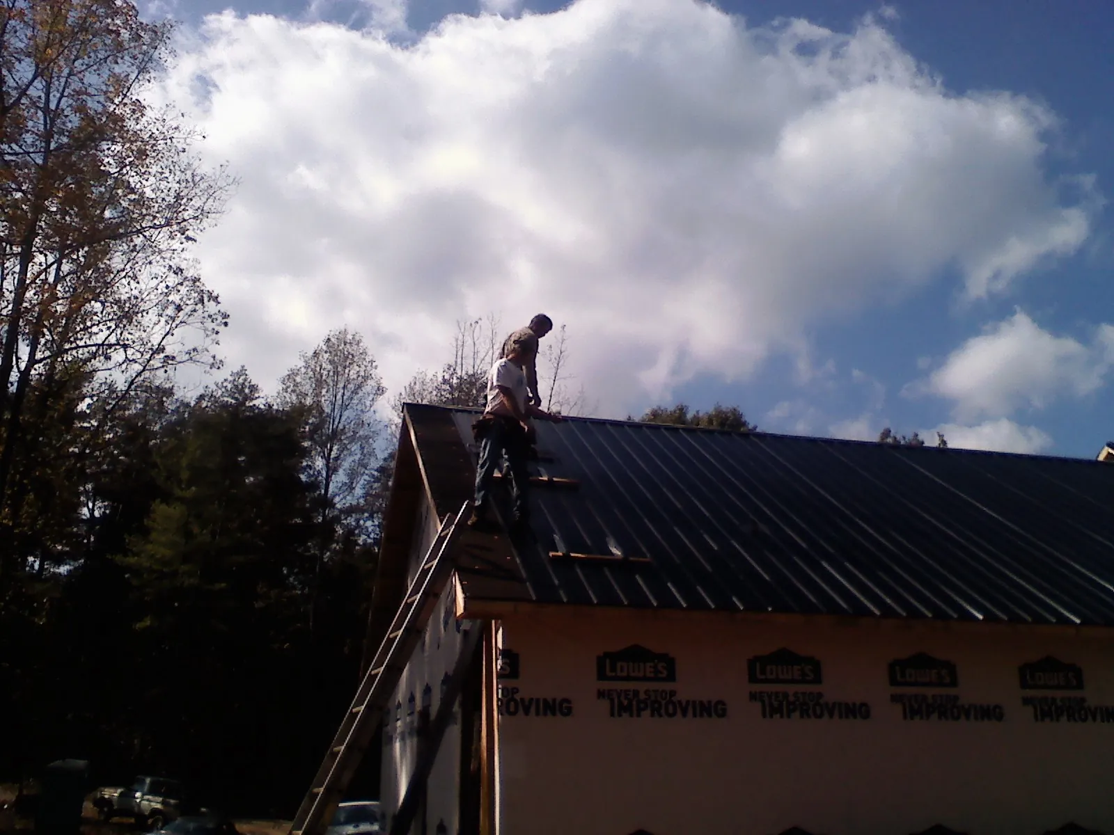 Roofer fastening dark metal panels high against a cloudy sky, from a Roof Inspection job in Cheyenne